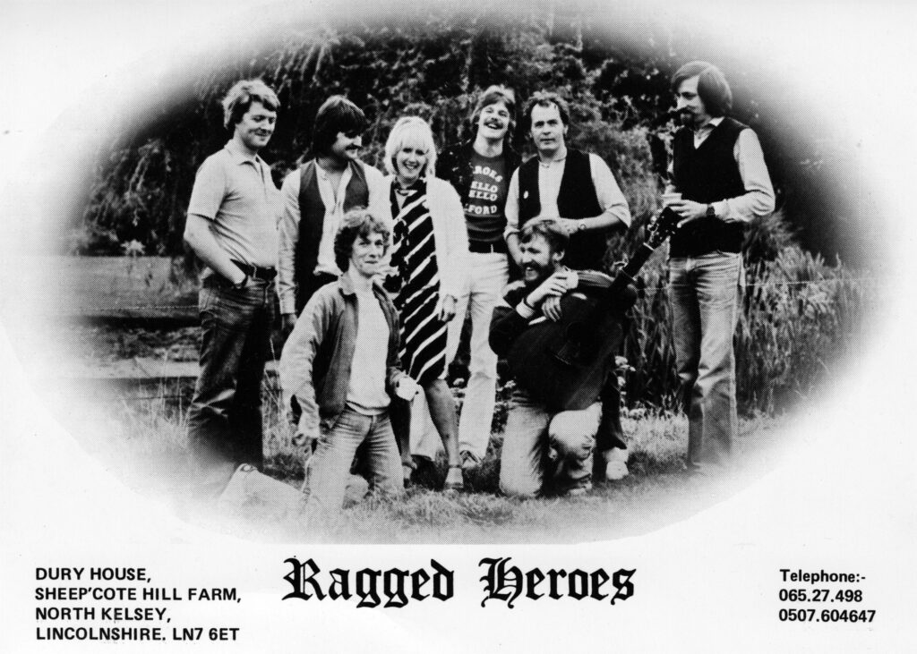 A postcard photo of the folk rock band 'Ragged Heroes’, showing the members Jeremy Sharpley, Paul Ogden, Vikki Clayton, John Skrypniuk, Johnny Tasker, John Hart, Ian Leese, and Stephen Clayton.